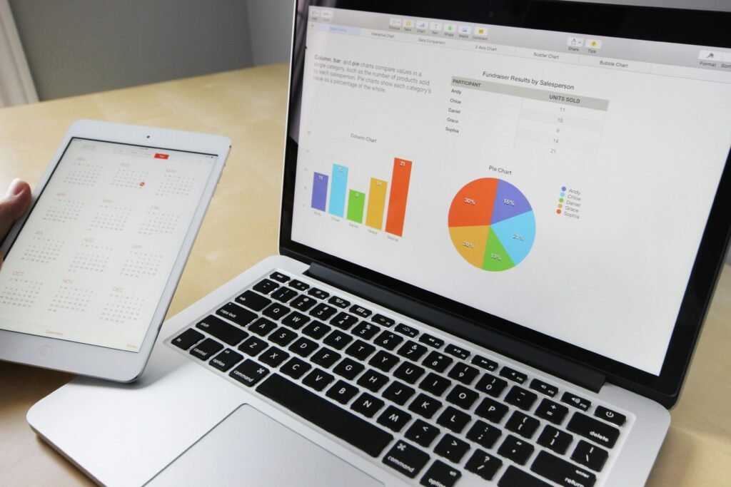 Laptop exibindo tabelas e gráficos com calendário de tablet para análise e planejamento de dados.