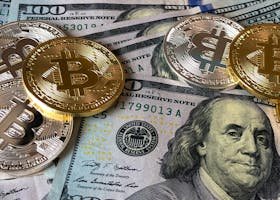 Moedas de Bitcoin sobre notas de cem dólares americanos, simbolizando a relação entre criptomoedas e moedas tradicionais.