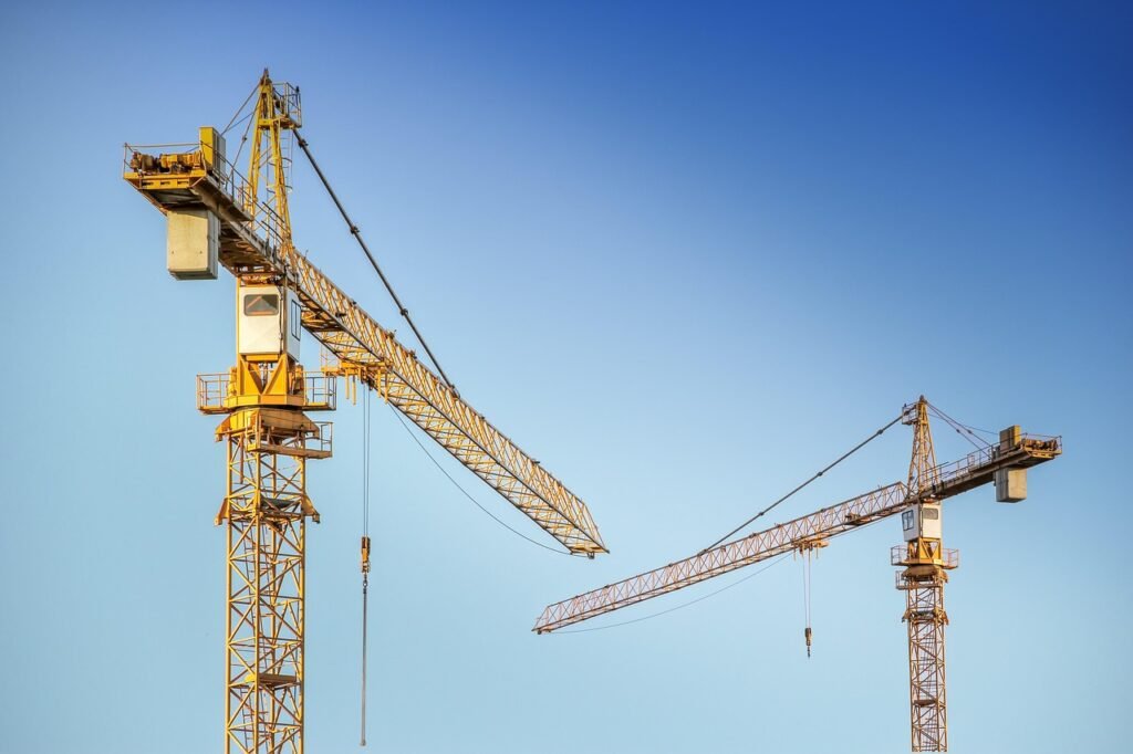Dois guindastes amarelos de construção civil em operação contra um céu azul claro, representando o desenvolvimento imobiliário e a expansão do setor de construção que impacta o mercado de fundos imobiliários.