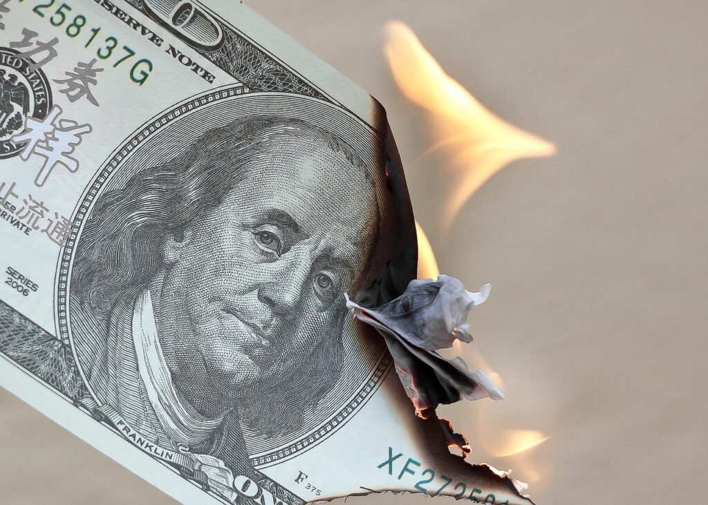 Nota de cem dólares americanos queimando em chamas na borda direita, simbolizando a perda de valor do dinheiro devido à inflação.