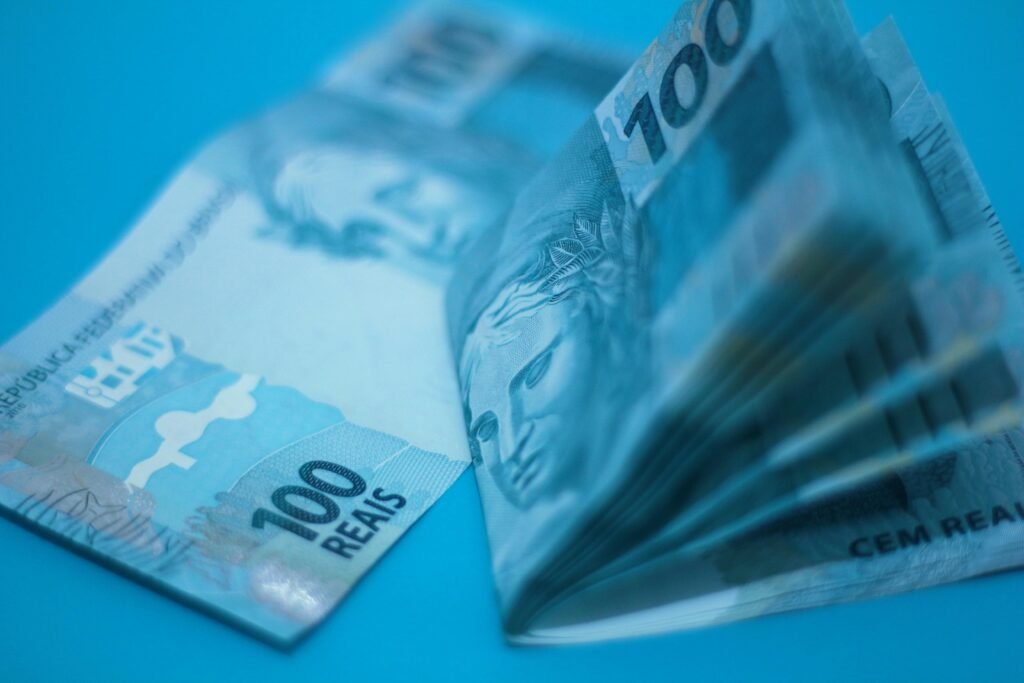 Pilha de 100 notas reais brasileiras colocadas em uma superfície azul, mostrando detalhes das notas.